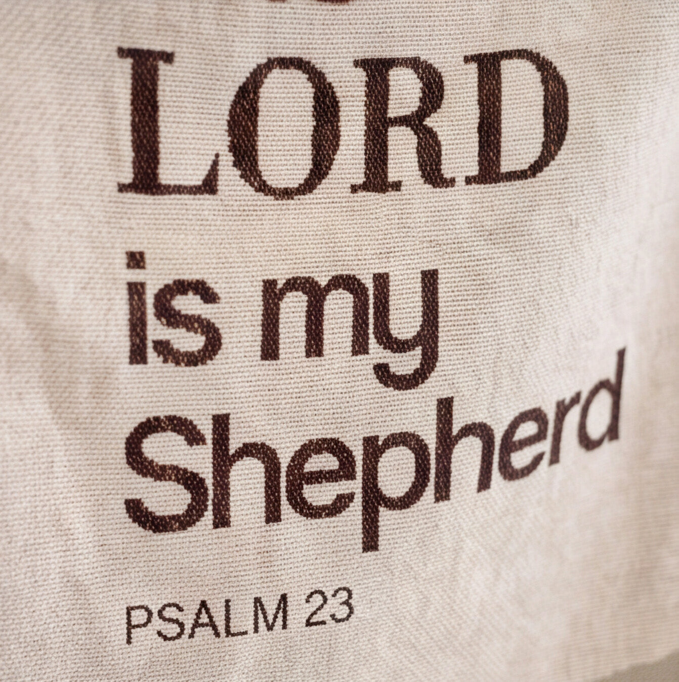 Close-up of a beige fabric item printed with the phrase 'LORD is my Shepherd' and 'PSALM 23' in dark brown lettering.