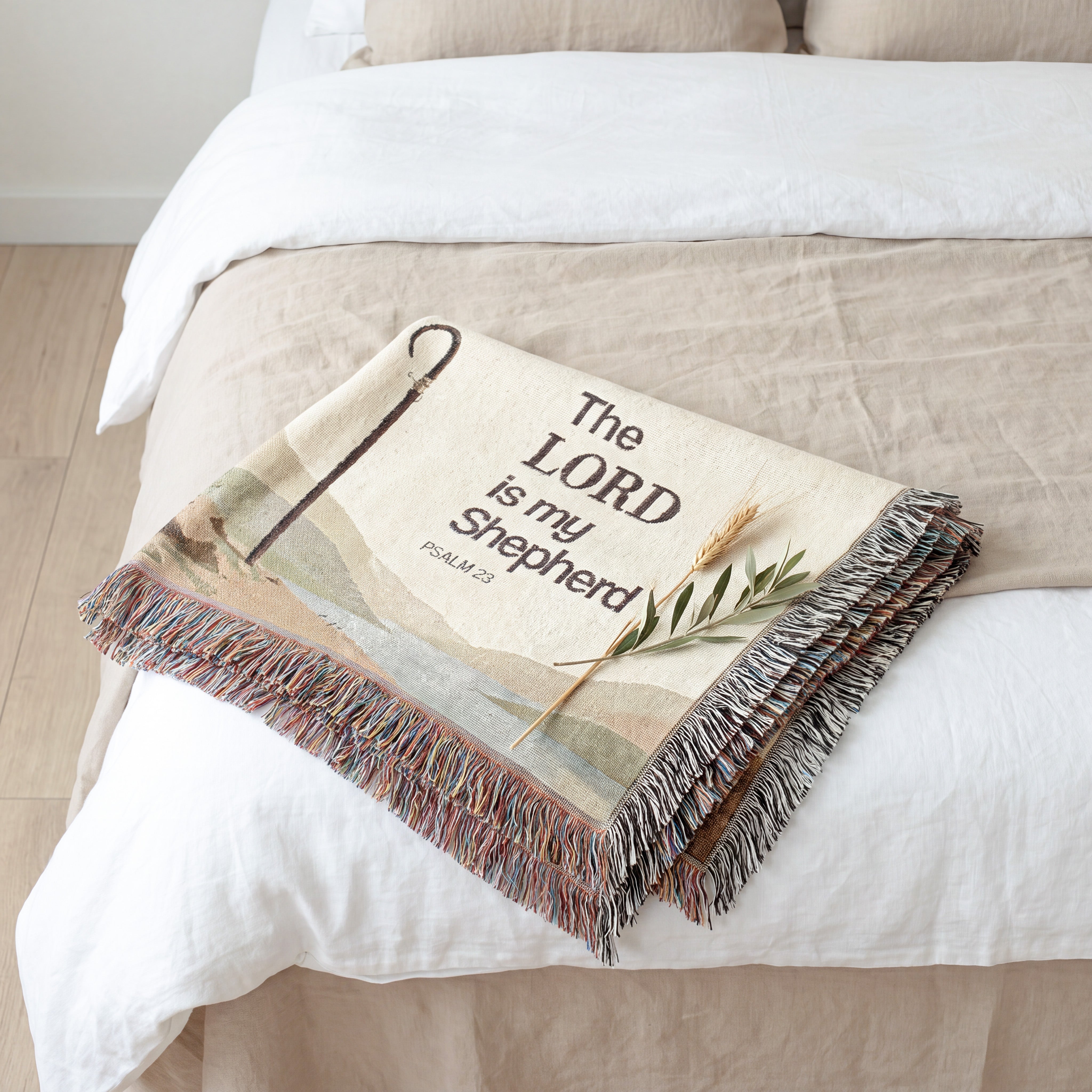A woven throw blanket with multicolor fringe and the text 'The LORD is my Shepherd' draped over a bed with white and beige bedding.
