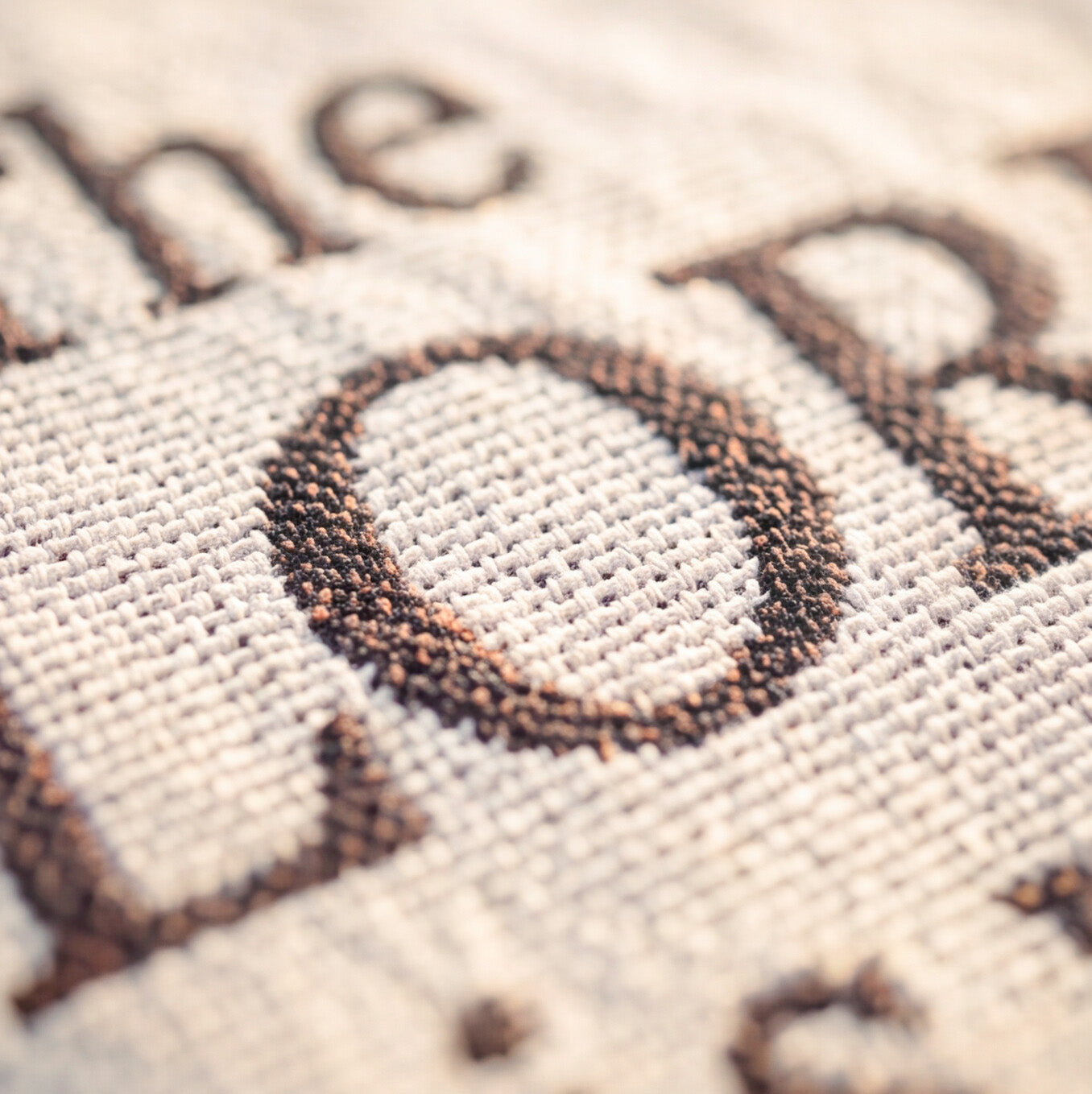 Close-up of a woven textile with dark brown embroidered lettering on a light beige fabric background.